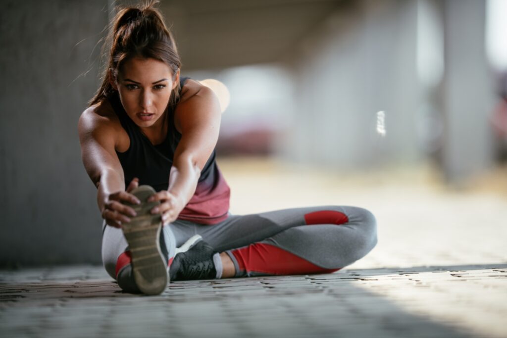 A woman using CBD for athletes stretches her legs on the ground.