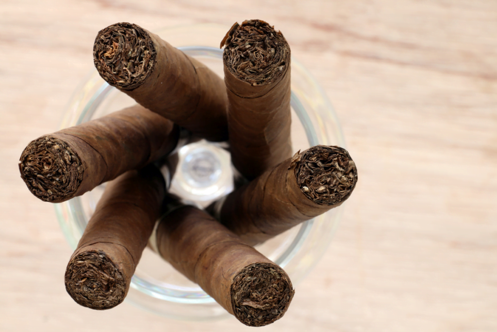 A group of cured tobacco cigars in a glass on a wooden table.