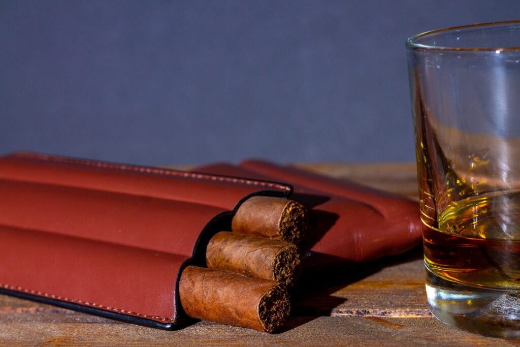 Stocking stuffer ideas for men: Cigars and a glass of whiskey on a wooden table.