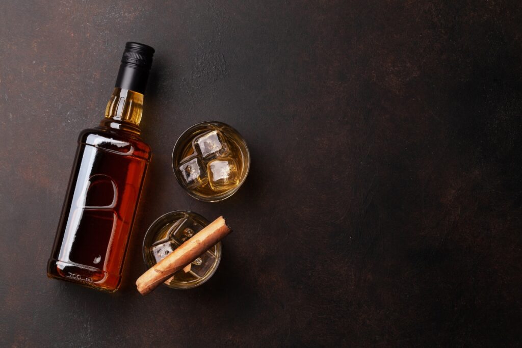 A bottle of whiskey with cinnamon sticks on a dark background, perfect for cigar gift ideas.