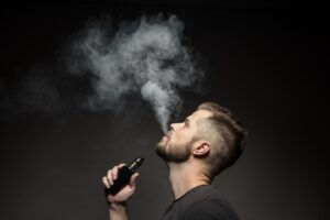 A man is using a vape starter kit to smoke an electronic cigarette on a black background.