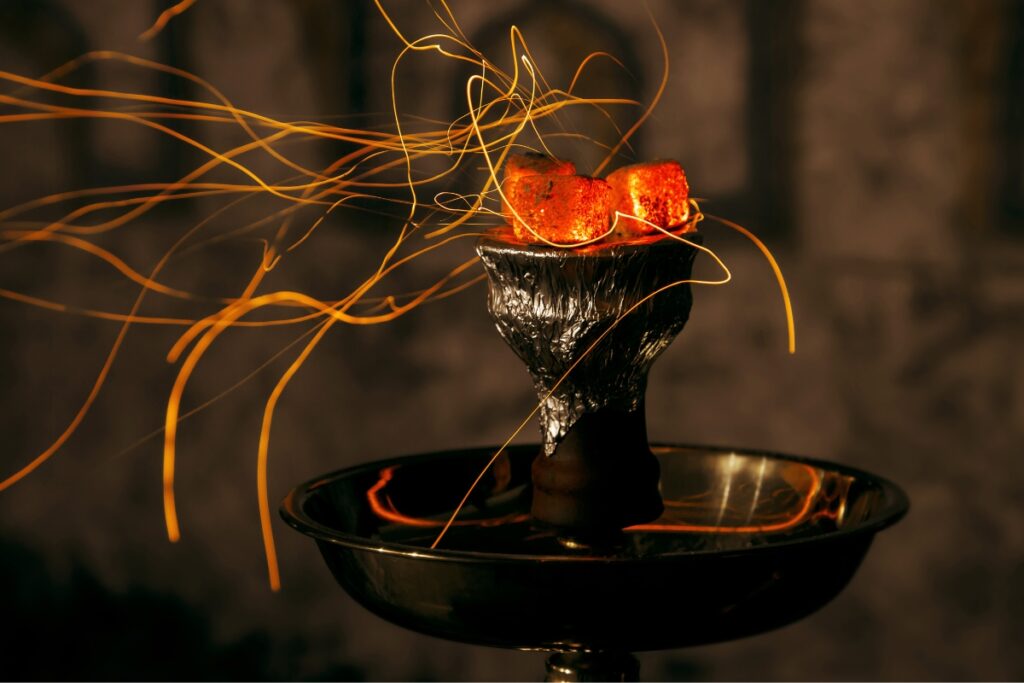 A candle is burning on a table surrounded by hookah flavors in front of a dark background.