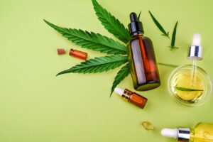 Flat lay of organic cbd oil bottles, gummies, and capsules with a marijuana leaf on a green background.