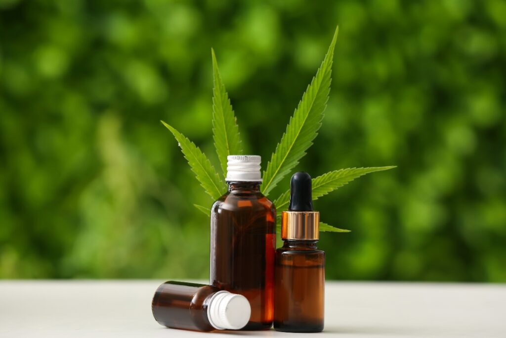 Organic cbd oil bottles with cannabis leaves on a table against a green background.