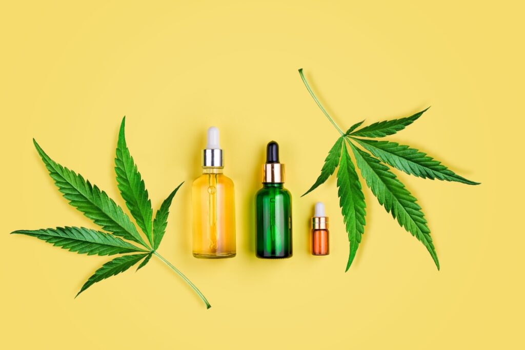 Three organic cbd oil bottles of varying sizes placed symmetrically between cannabis leaves on a bright yellow background.