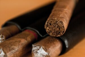 Three cigars, rich in tobacco history, partially wrapped in plastic, displayed on a table, focusing on the textured ends of the cigars.