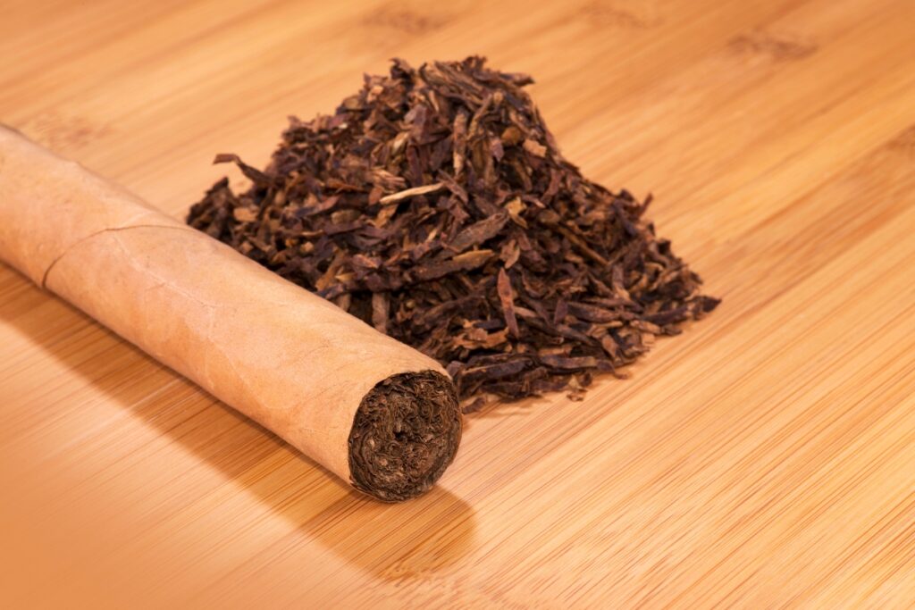 A cigar next to a pile of loose tobacco on a wooden surface, highlighting the impact of tobacco industry regulations.