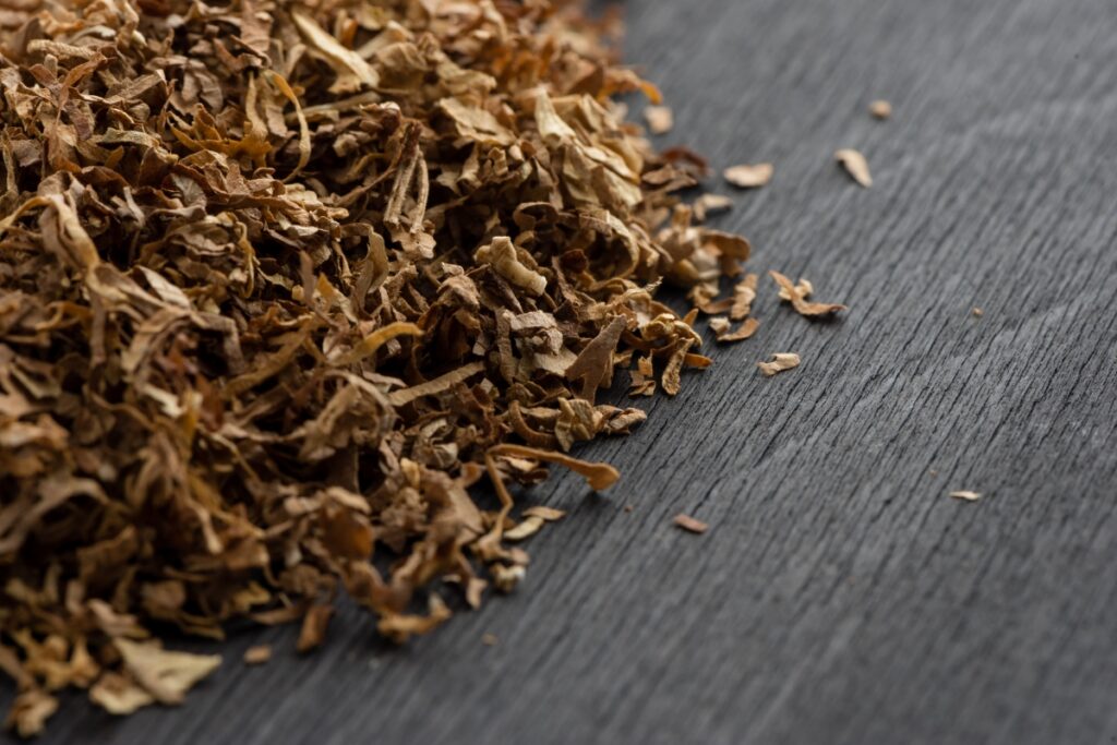 Close-up of dried tobacco leaves impacted by industry regulations scattered on a dark wooden surface.