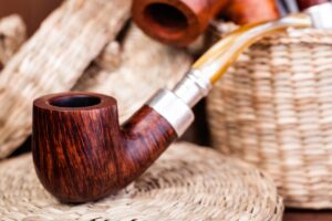 A close-up of a wooden smoking pipe with a metal ring and curved stem, sitting on a woven basket, evokes the tradition cherished by modern pipe smokers.