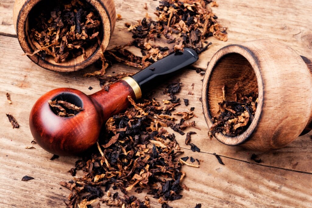 A wooden smoking pipe rests on a wooden surface, surrounded by loose tobacco and two open wooden containers filled with tobacco, capturing the essence of modern pipe smokers' rituals.