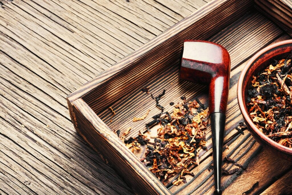 A wooden pipe and a bowl with loose tobacco rest on a wooden surface, evoking nostalgia among modern pipe smokers.