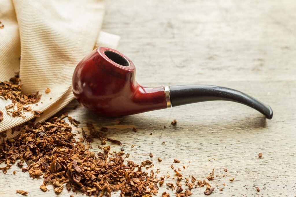 A wooden smoking pipe rests on a wooden surface with scattered tobacco and a cloth nearby, a classic scene that resonates with modern pipe smokers.