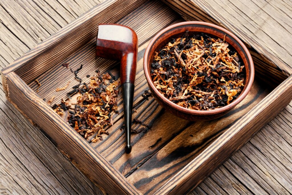 Wooden pipe and bowl filled with tobacco shavings on a wooden tray, catering to modern pipe smokers.