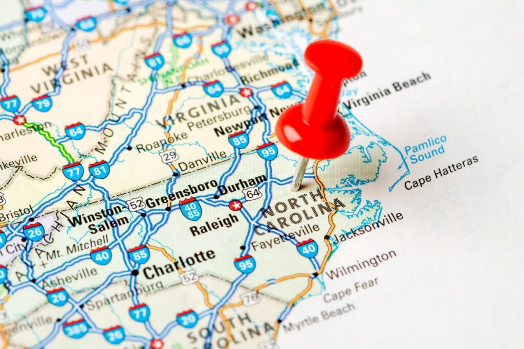 A detailed map of North Carolina, one of the prominent tobacco-producing states, with a red pushpin marking a location near its center. The map displays various cities, highways, and neighboring states.