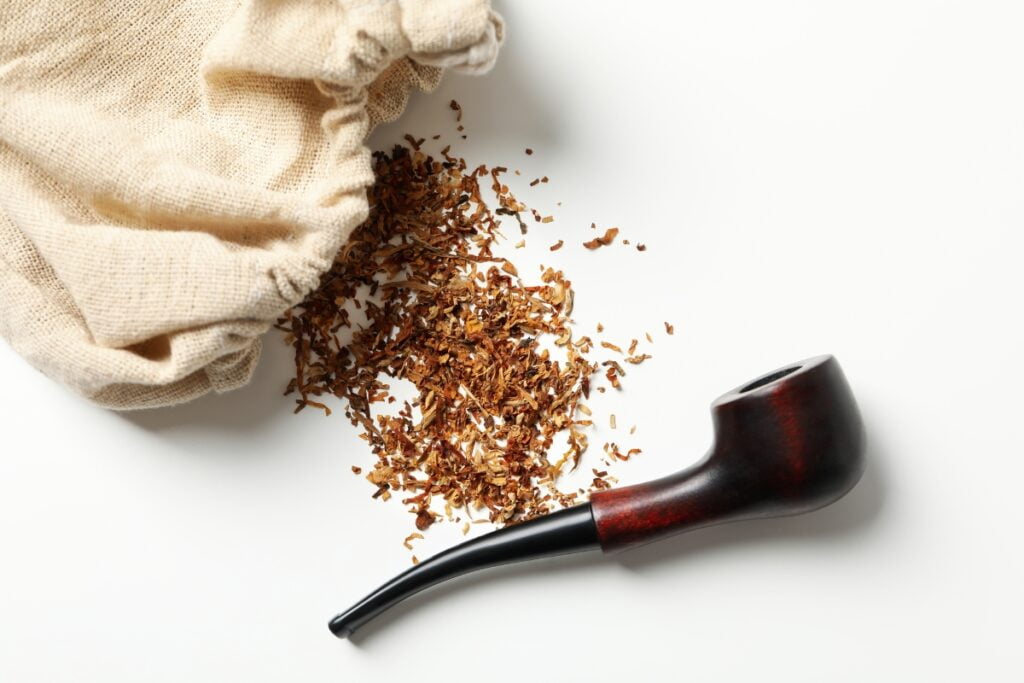 A tobacco pipe rests next to a burlap sack, with a small pile of loose tobacco—harvested from one of the leading tobacco producing states—spilled out onto a white surface.