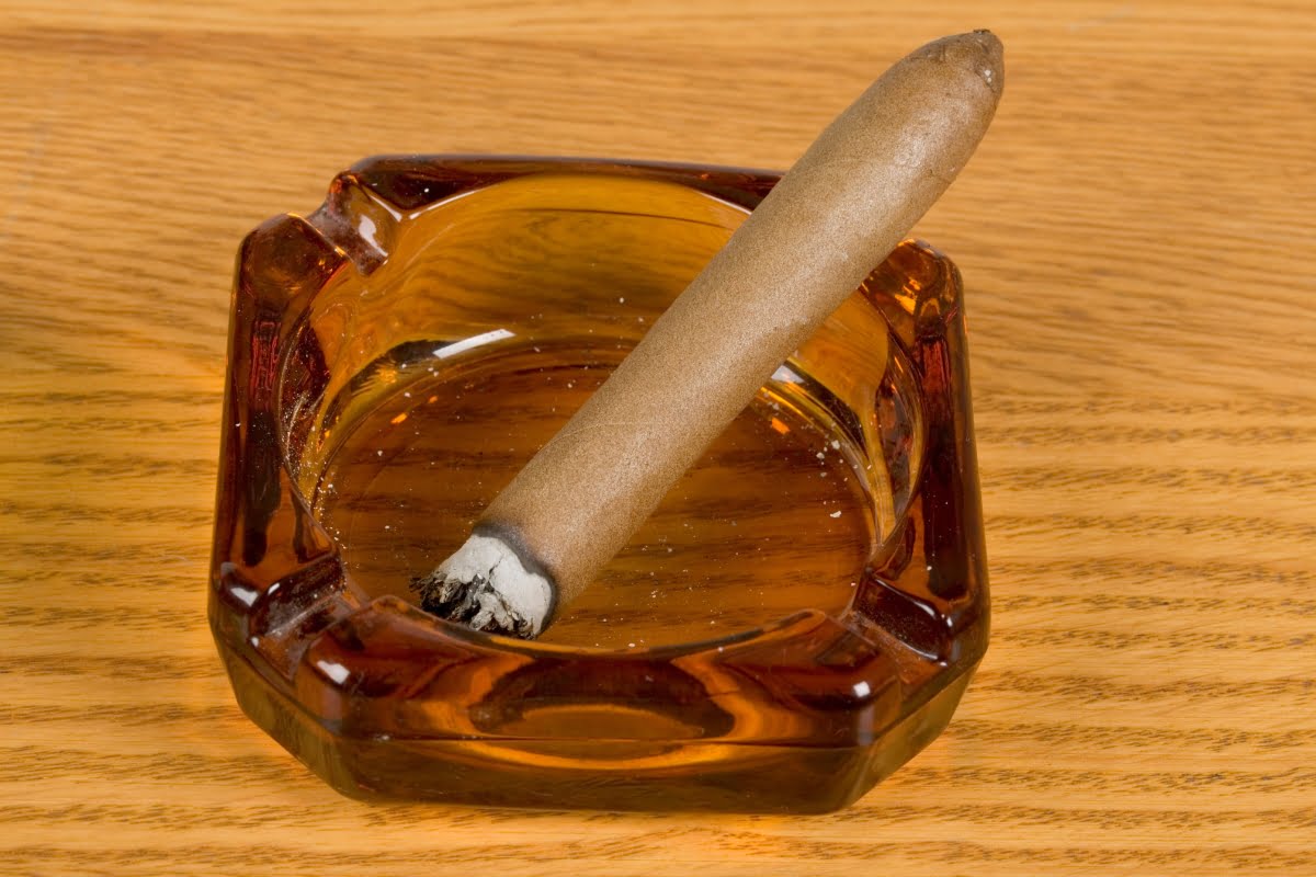 A lit cigar rests on a brown glass ashtray placed on a wooden surface, capturing the essence of a true smoking enthusiast's haven.