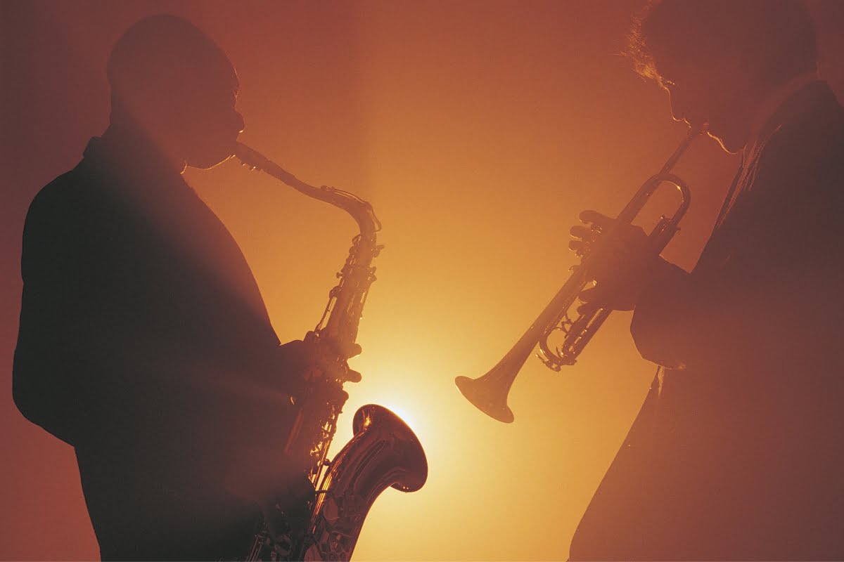 Two musicians silhouetted against an orange background, one playing a saxophone and the other playing a trumpet, like they're in an intimate smoking session.