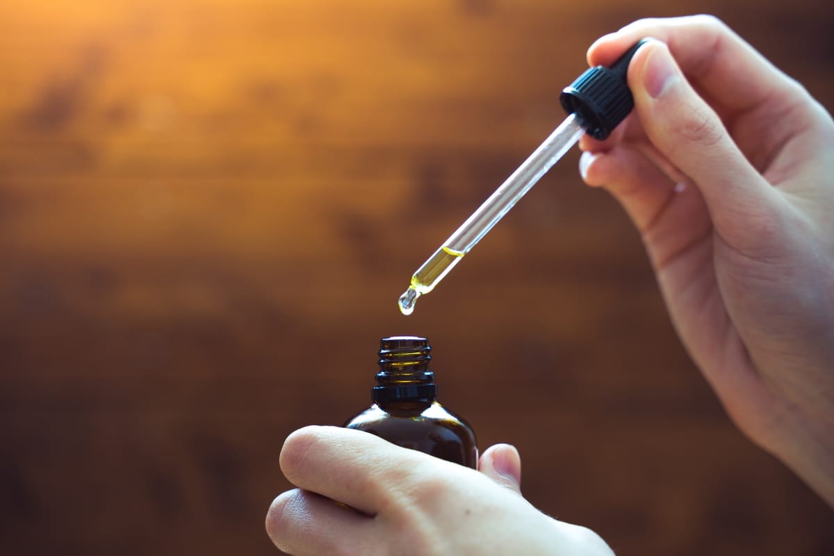 Hands holding a dropper above a small brown bottle with liquid, ready to dispel CBD myths.