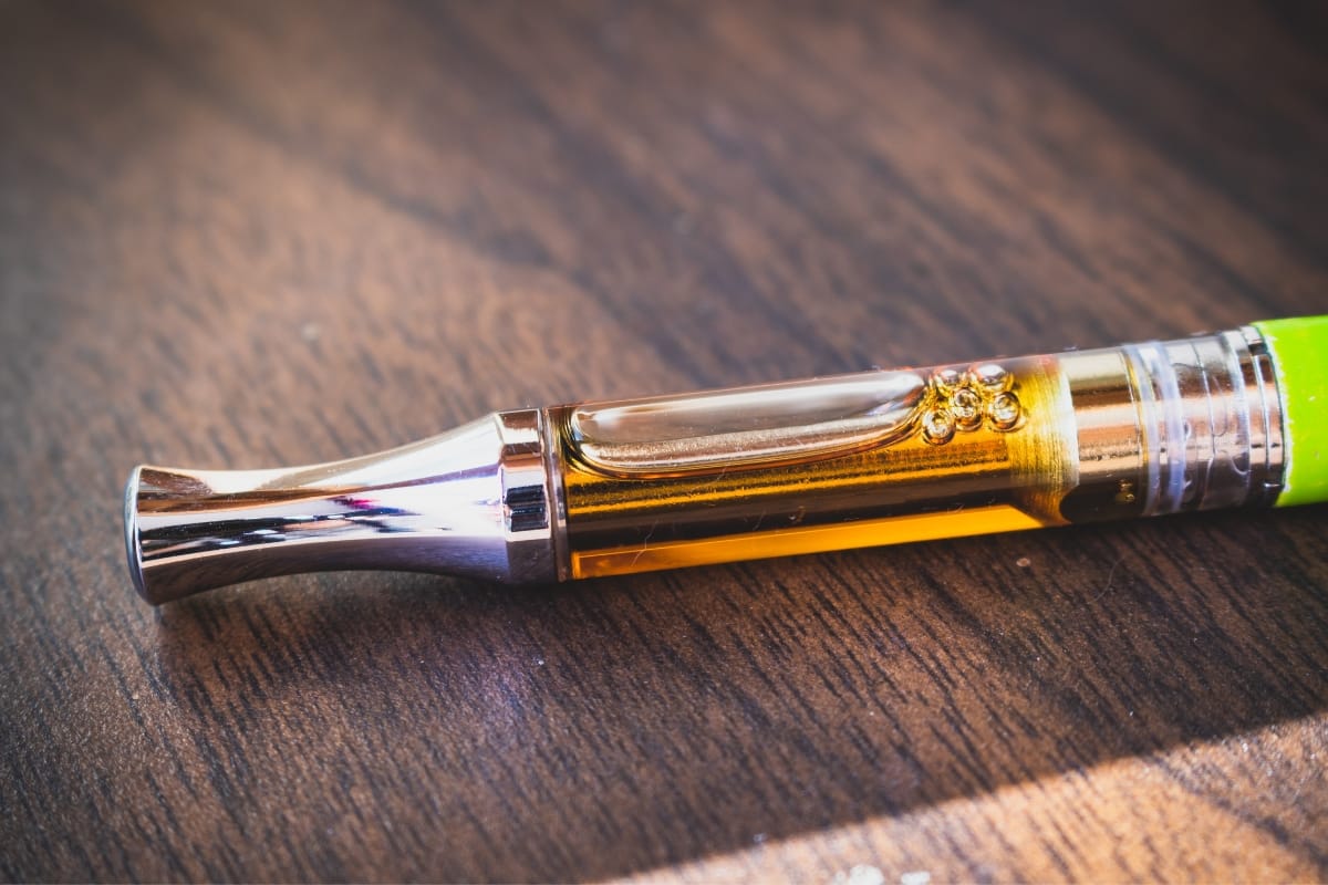 A CBD vape pen with a metal mouthpiece and visible liquid chamber rests elegantly on a wooden surface.