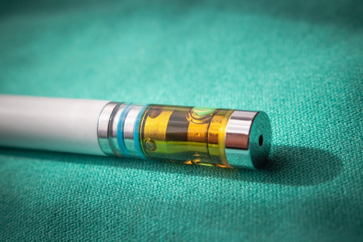 Close-up of a CBD vape pen cartridge with a metal tip resting on a green fabric surface. The cartridge is partially filled with amber liquid, highlighting its sleek design.