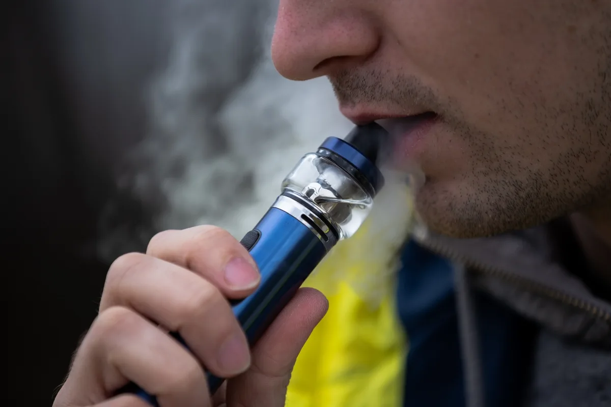 Close-up of a person inhaling from a blue vaping device, producing visible vapor, highlighting the modern allure of vape technology when compared to traditional hookah experiences.